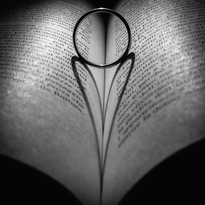 A ring casts a heart shadow on an open book in a conceptual black and white photo.